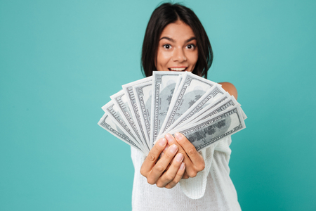 Happy excited young woman holding bunch of united states dollars over blue backgroundの写真素材