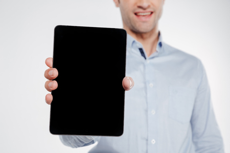Cropped image of smiling man in shirt which showing blank tablet computer screen at camera. Isolated white backgroundの写真素材