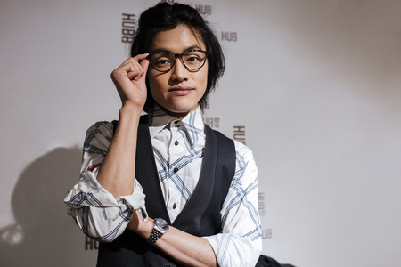 Photo of attractive young asian man wearing glasses dressed in jacket and shirt standing indoors and looking at camera. Coworking concept.の写真素材