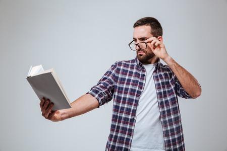 Bearded man in eyeglases which reading book. Isolated gray backgroundの写真素材