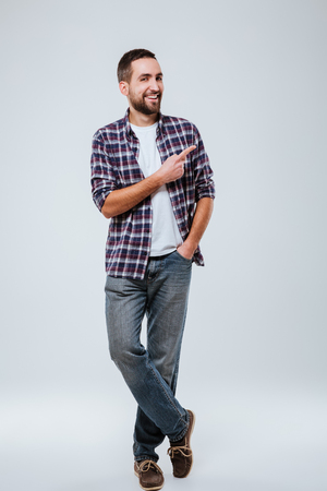 Full length portrait of Bearded man in shirt with arm in pocket which pointing away. Isolated gray backgroundの写真素材