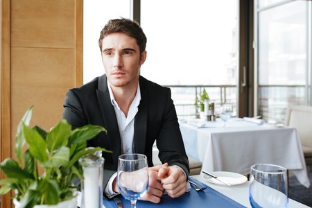 Serious Man in suit which sitting by the table in restaurant and looking awayの写真素材