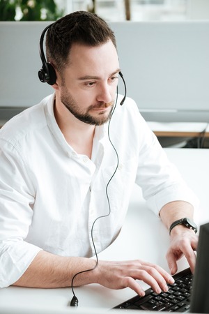 Vertical image of Man in shirt and headset which sitting by the table and using computer