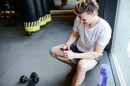 Side view of muscular man which using smartphone and sitting near window in gymの写真素材