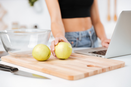 Cropped image of woman which standing by the table with apple and laptop in kitchenの写真素材