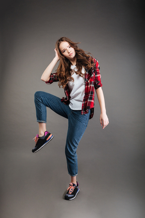 Serious young woman in plaid shirt and jeans dancing over grey backgroundの写真素材
