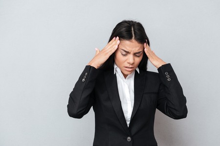 Business woman in suit which having headache. Isolated gray background