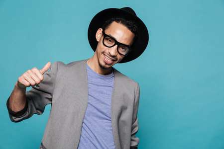 Portrait of a smiling stylish african man in eyeglasses showing thumbs up gesture over blue backgroundの写真素材