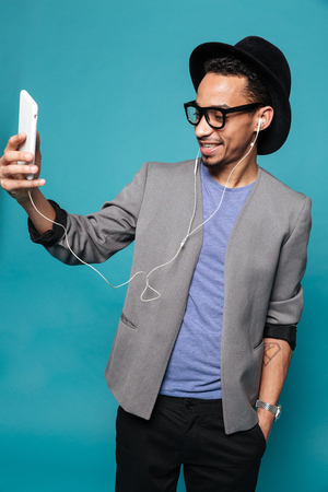 Young handsome african man in sunglasses listening music in headphones over blue backgroundの写真素材