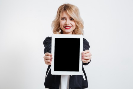 Photo of cheerful young lady standing over white background showing display of tablet computer to camera. Focus on display.の写真素材