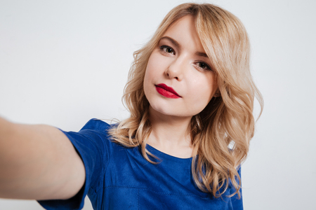 Photo of amazing young lady dressed in blue dress make selfie and posing over white background.の写真素材