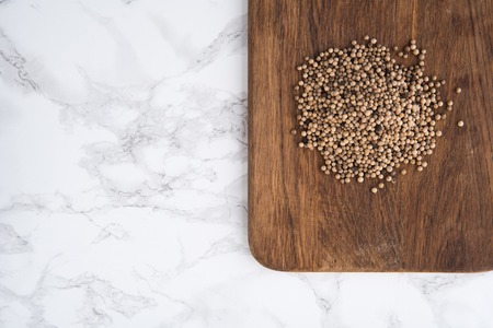 Top view of a spicy white peppercorns heap on a wooden cutting board on white marble backgroundの写真素材