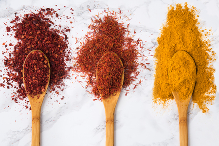 Top view of an assortment of colorful spices in the wooden spoons on the white marble backgroundの写真素材