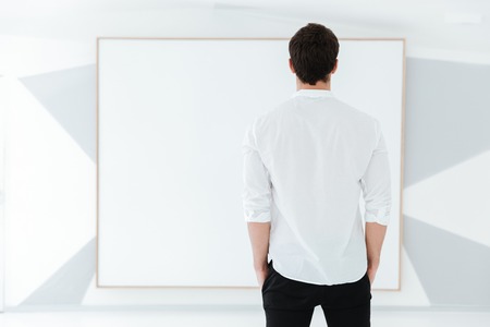 Back view of man dressed in white shirt standing near big board.の写真素材