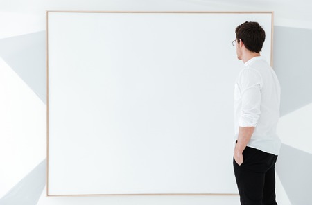 Side view of man wearing eyeglasses and dressed in white shirt standing near big board.の写真素材