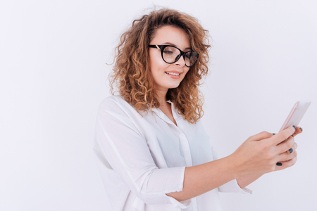 Side view of Woman in glasses and white shirt making selfie on phone. Isolated gray backgroundの写真素材