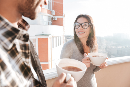 Image of young happy couple drinking coffee while standing on roof. Look at each other.の写真素材
