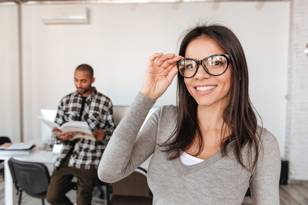 Image of young business partners standing in office while man holding magazine and woman look at camera. Focus on woman.の写真素材
