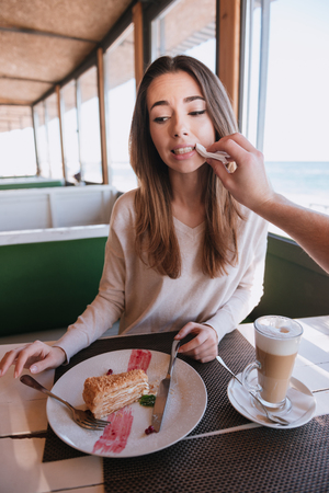 Verical image of attractive woman sitting by the table with food on date in cafe near the sea and her man wipes her cheek. First-person viewの写真素材