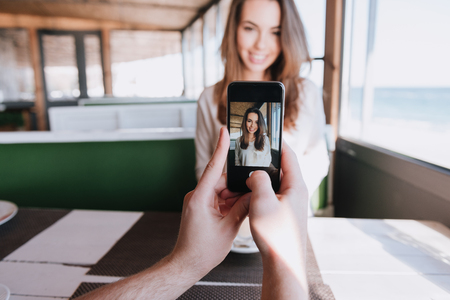 First-person view of man making photo on phone his smiling woman on date in cafe near the seaの写真素材