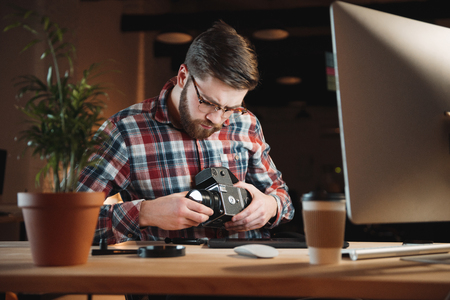 Portrait of a young bearded man repairing an old camera at his workplaceの写真素材