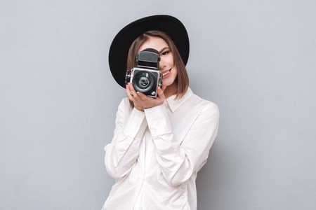 Portrait of a young smiling woman filming with retro camera isolated on the gray backgroundの写真素材