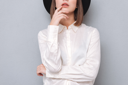 Cropped image of a young stylish woman in hat and shirt posing isolated on a gray backgroundの写真素材