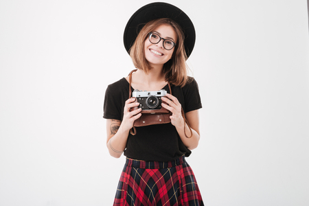 Portrait of a charming smiling woman in hat holding retro camera isolated on a white backgroundの写真素材