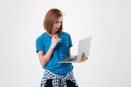 Portrait of a young casual girl standing and holding laptop screen isolated on a white backgroundの写真素材