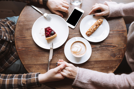 Top view picture of loving young couple sitting at the cafe and eating cakes drinking coffee.の写真素材