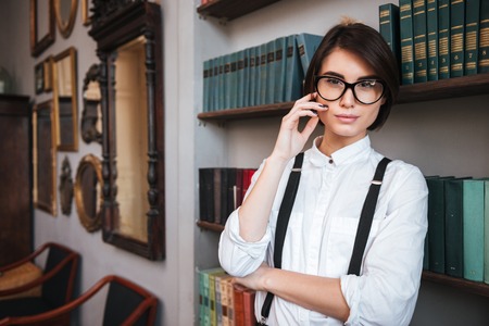 Authoress in glasses and white shirt standing near the bookshelf and looking at cameraの写真素材