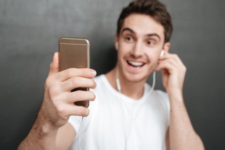 Close up of Man listening music on phone in studio. Focus on phone. Isolated dark backgroundの写真素材