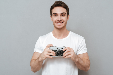 Smiling man holding retro camera in hands and looking at camera. Isolated gray backgroundの写真素材