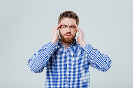 Tensed bearded young man touching his temples and having headache over white backgroundの写真素材