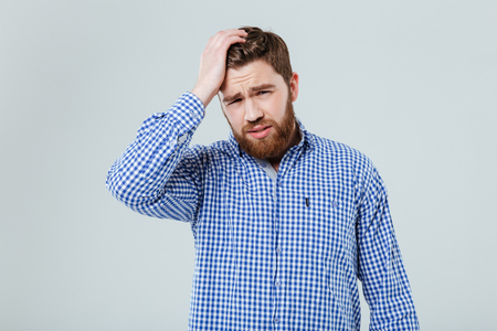 Sad bearded young man with hand on head having headache over white backgroundの写真素材