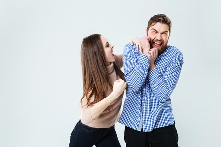 Mad aggressive young woman shouting and fighting with her husband over white background