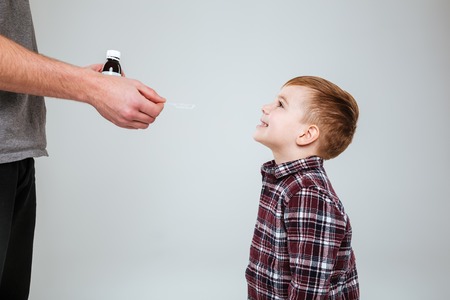 Young boy taking medications from father. Isolated gray backgroundの写真素材
