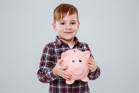 Smiling Young boy with moneybox in hands looking at camera. Isolated gray backgroundの写真素材