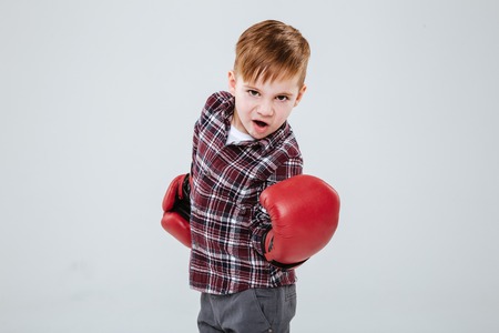 Cool little boy in red boxing gloves standing and training over white backgroundの写真素材