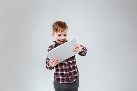 Picture of little cute child standing over grey background holding tablet computer. Look at tablet.の写真素材
