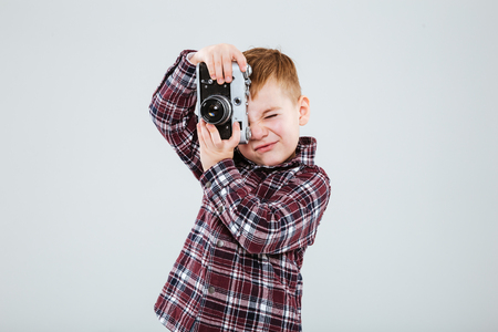 Little boy standing and taking pictures with old vintage photo camera over white backgroundの写真素材