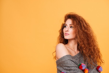 Portrait of a pensive young red hair woman thinking and looking away isolated on orange backgroundの写真素材