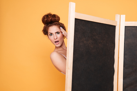 Amazed pretty young woman standing behind folding screenの写真素材