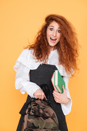 Cheerful curly young woman holding backpack and booksの写真素材