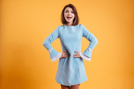 Happy excited young woman standing with hands on waist over yellow background