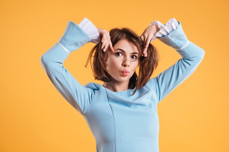 Playful comical young woman joking and making funny face over yellow backgroundの写真素材