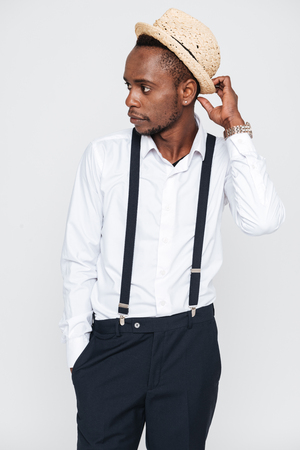 Image of handsome african man wearing hat posing in studio. Isolated over white background. Look aside.の写真素材