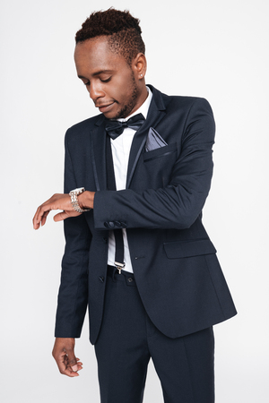 Image of young handsome african businessman posing in studio. Isolated over white background. Look at watch.の写真素材