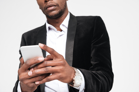 Cropped image of attractive african businessman chatting by his phone. Isolated over white background.の写真素材