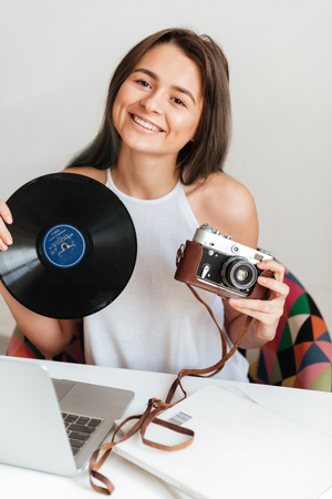 Photo of gorgeous happy casual woman working on a laptop sitting on the chair in the house while holding record and camera.の写真素材